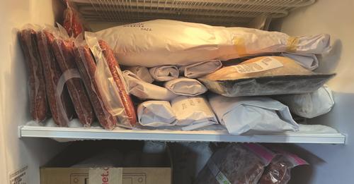 A shelf of a freezer contained stacks of meat wrapped in white paper with dates written on the paper. Photo by Erika Malo
